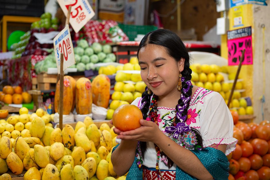 Woman in vibrant traditional attire admiring an orange at a bustling fruit market.