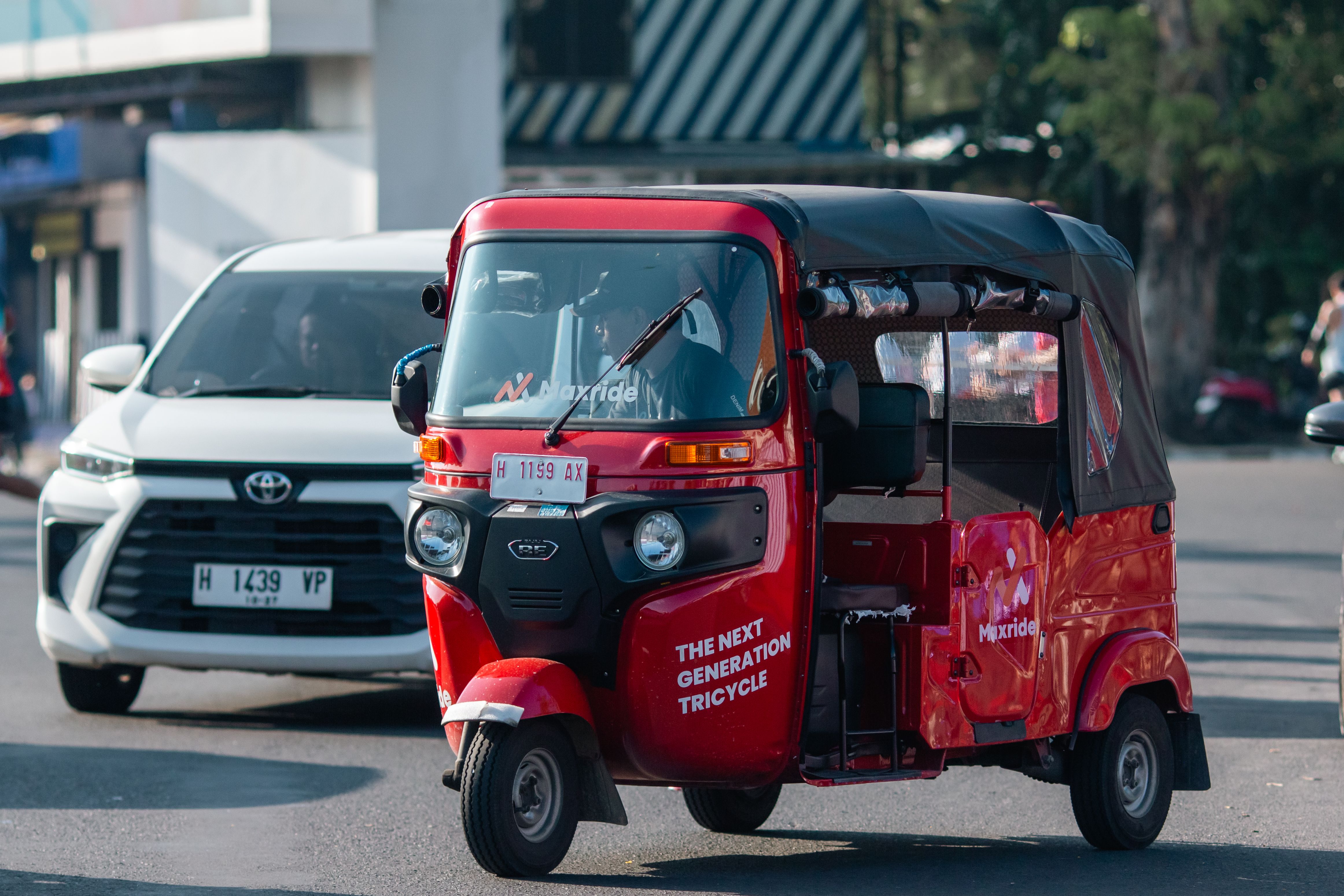 Red auto rickshaw navigating city traffic, showcasing urban transportation.