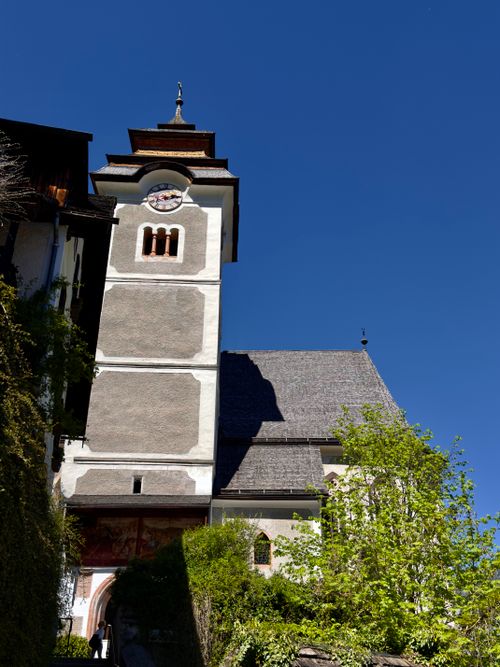 Free A charming church tower in Hallstatt, Austria against a clear blue sky, showcasing architectural beauty and greenery. Stock Photo