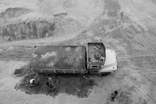 Black and white aerial photo capturing workers loading a truck in a sandy area.