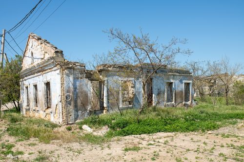 Free A sunlit abandoned building in Kerch, surrounded by overgrown grass and trees. Stock Photo