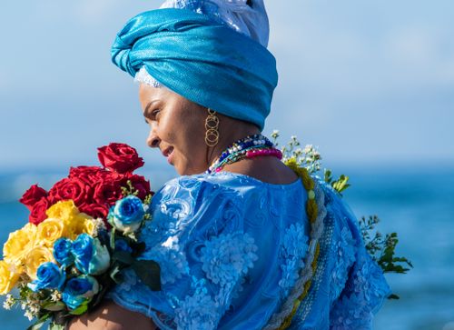 Free A woman in vibrant attire holds flowers, captured beautifully by the ocean. Stock Photo