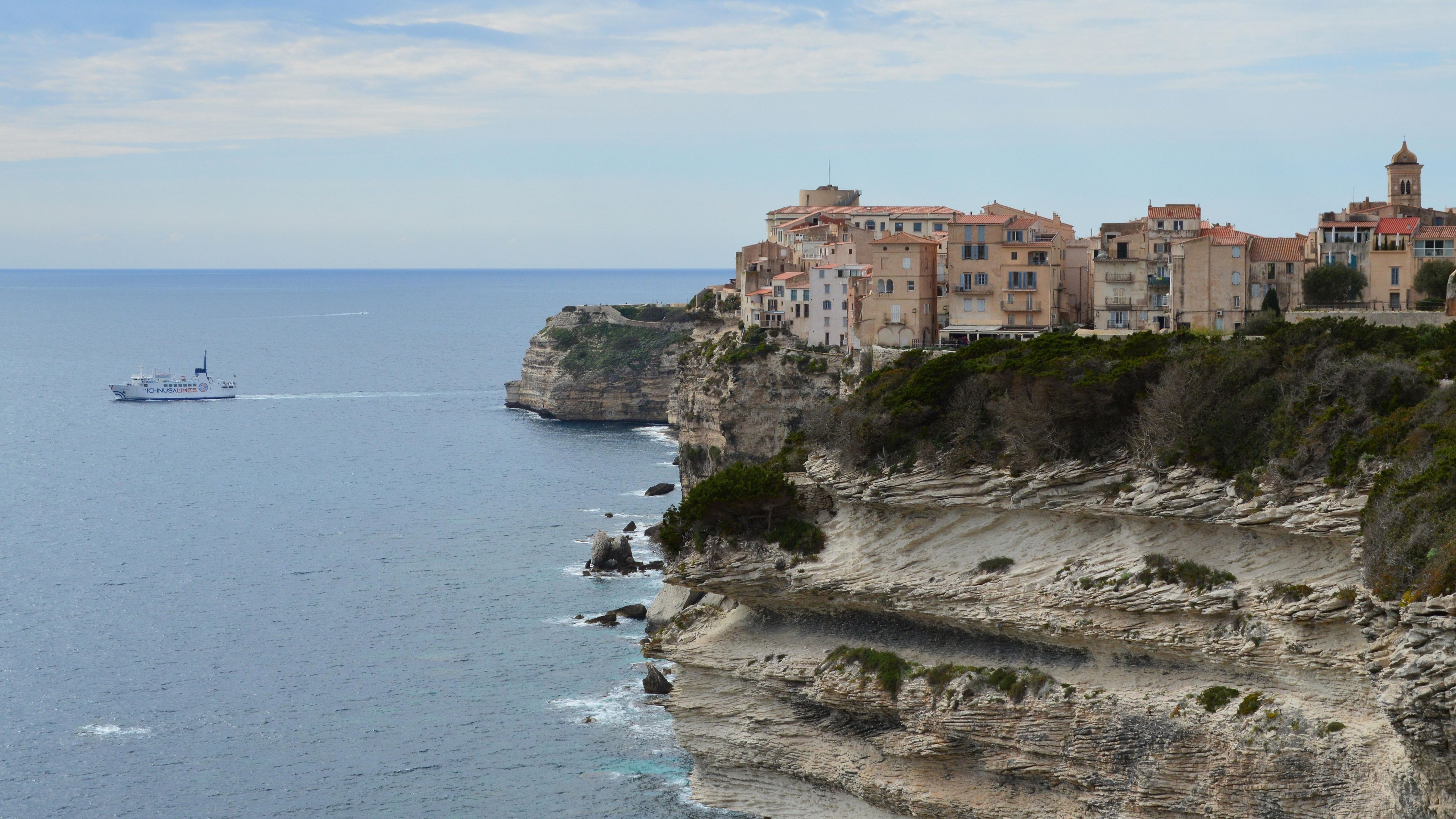 Dramatic view of Bonifacio's coastal cliffs and a ferry on the Mediterranean Sea.