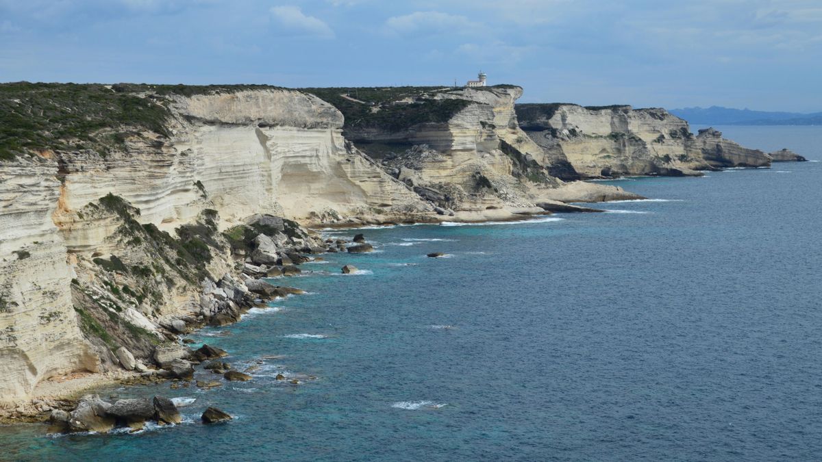Faleze albe verticale in sir, cu far pe promontoriu si apa turcoaz