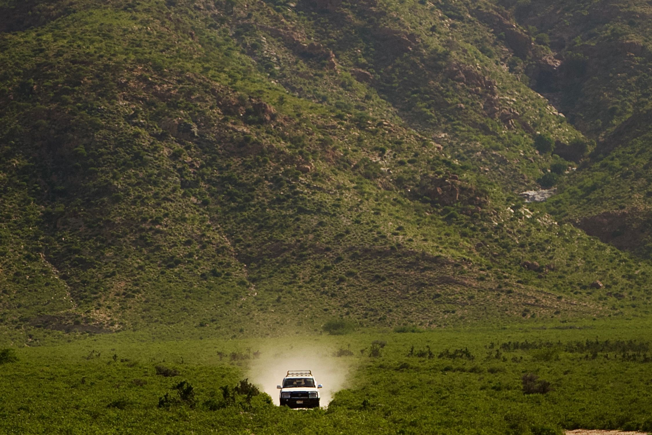 A lone off-road vehicle driving through lush green valley with mountain backdrop.