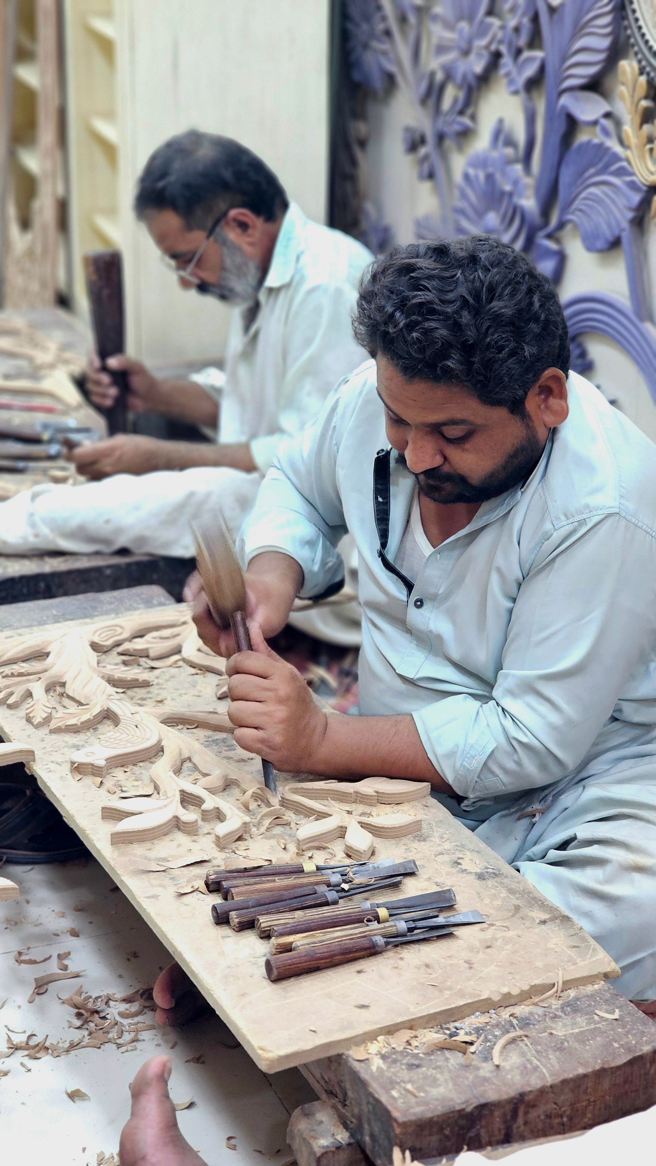 Artisans meticulously carving wood in a workshop, showcasing traditional craftsmanship.