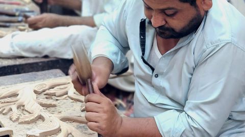 Artisans meticulously carving wood in a workshop, showcasing traditional craftsmanship.