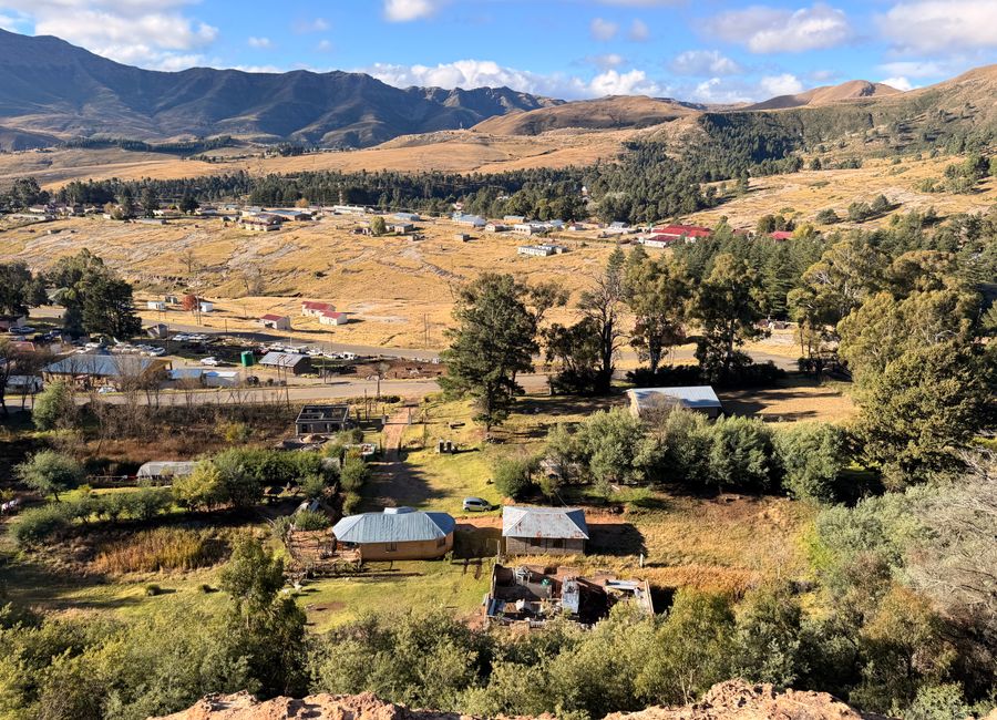 A picturesque aerial view of a rural village in Lesotho, surrounded by mountains and lush greenery.