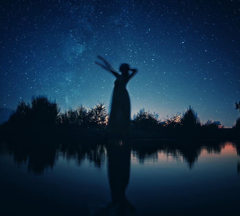 Free Silhouette of Woman Standing on Rock Near Body of Water during Night Time Stock Photo