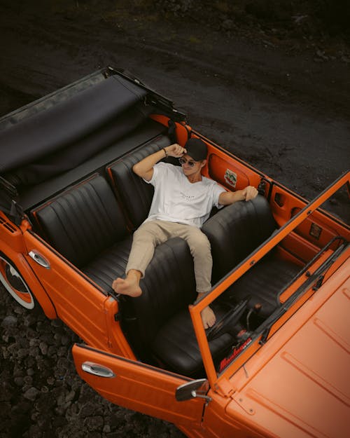 Man in White Shirt and Khaki Pants Lying in Orange Car
