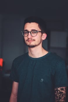 一位时尚的年轻男子，戴着眼镜，身上有纹身，风格清爽休闲