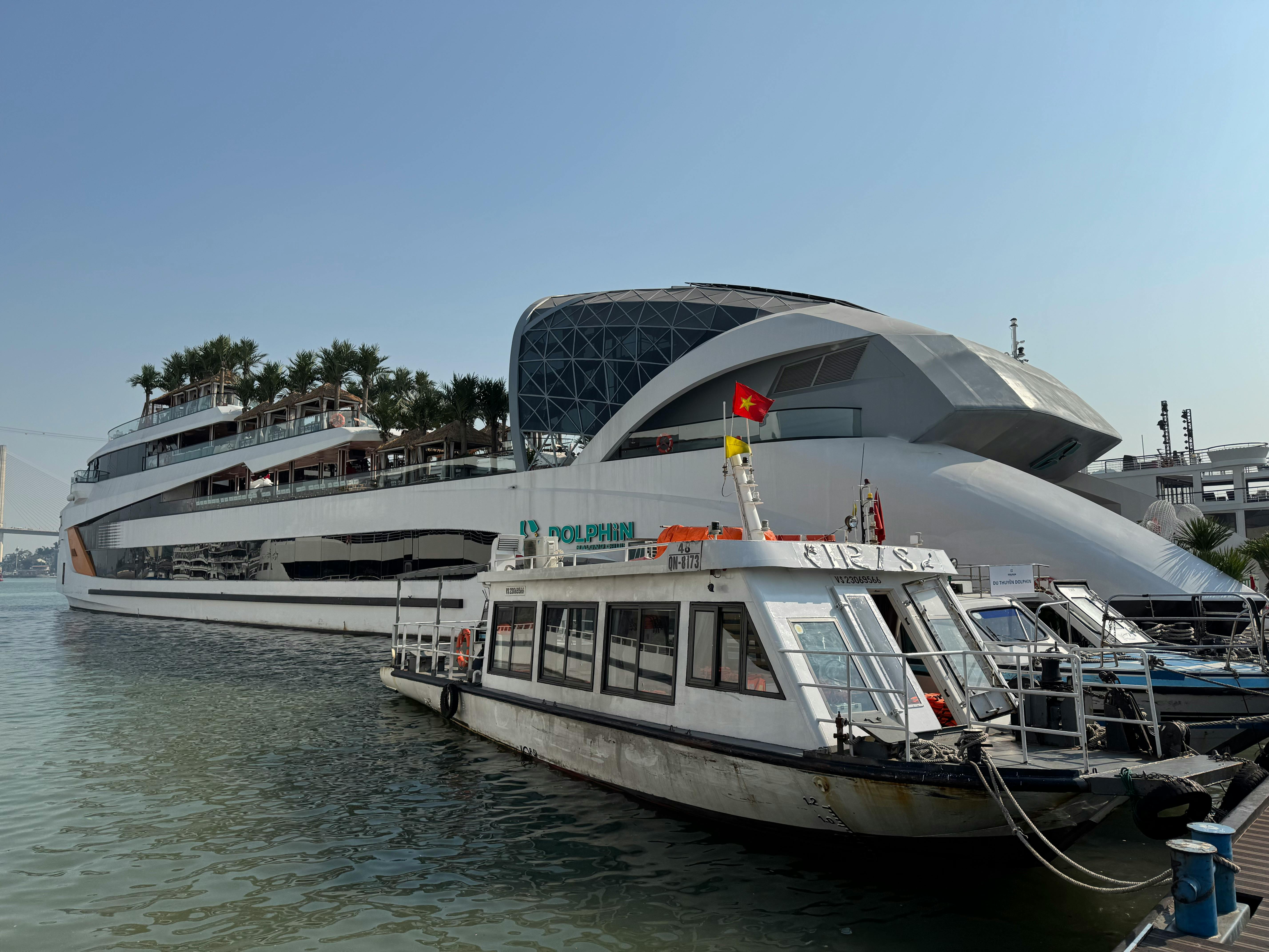 A sleek cruise ship docked alongside smaller boats in Tuan Chau harbor, Vietnam.