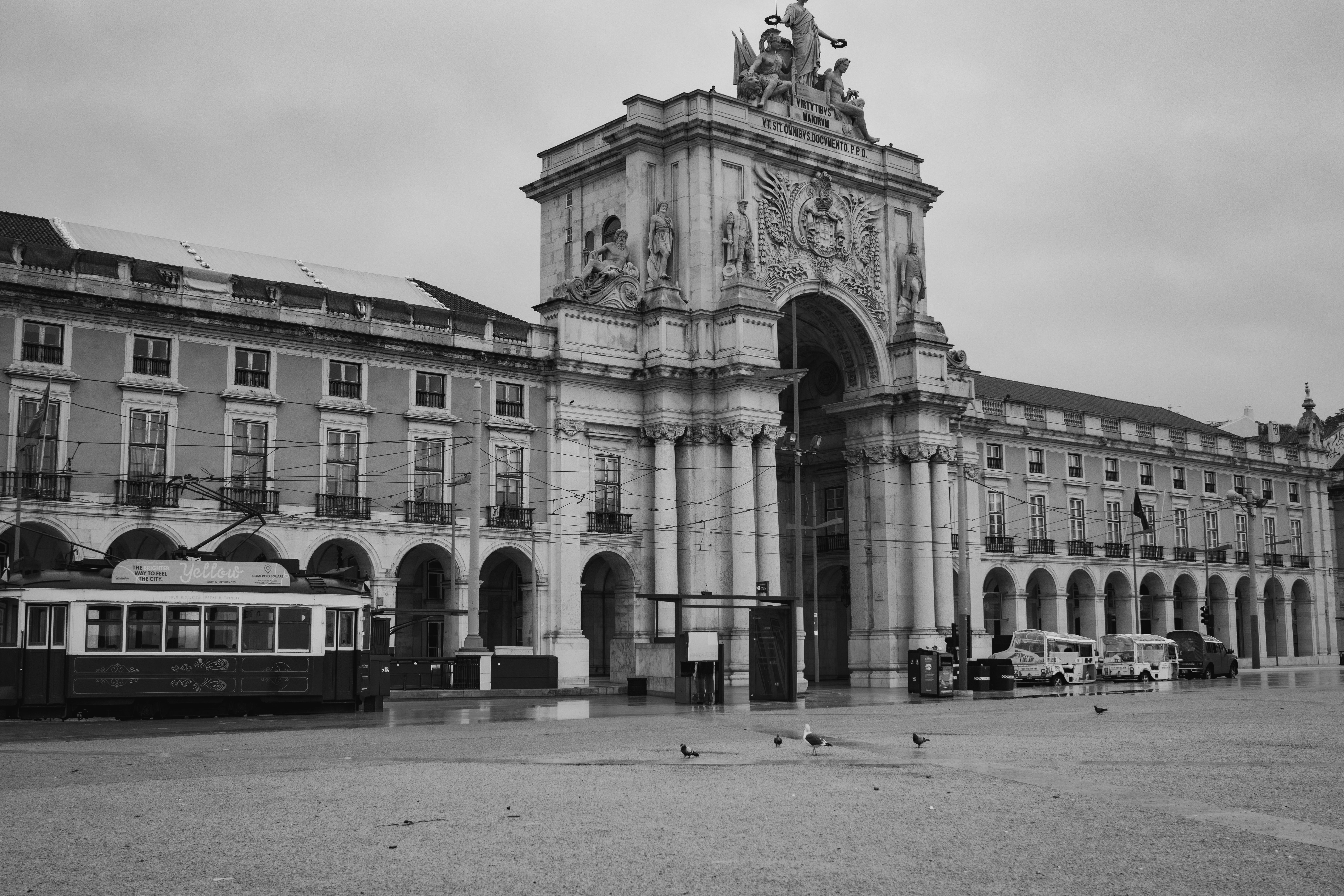A cream Lisbon taxi and a tuk-tuk waiting on a cobbled street near Praça do Comércio