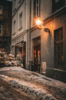 A cozy snow-covered street with a warm glowing lamp and shopfronts on a winter night.