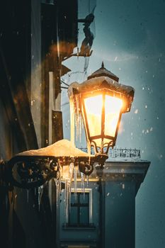Snow-covered streetlamp glowing warmly on a winter street with falling snow and icy details.