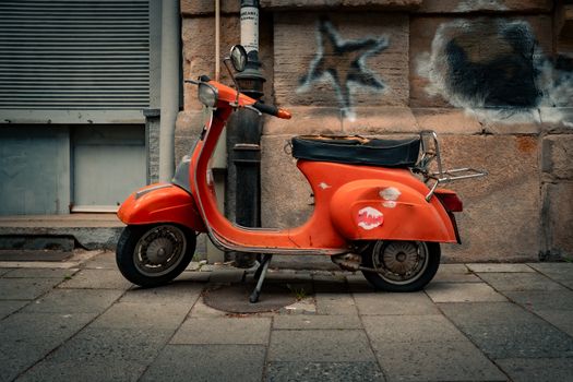 A weathered orange vintage scooter parked on a graffiti-adorned urban street.