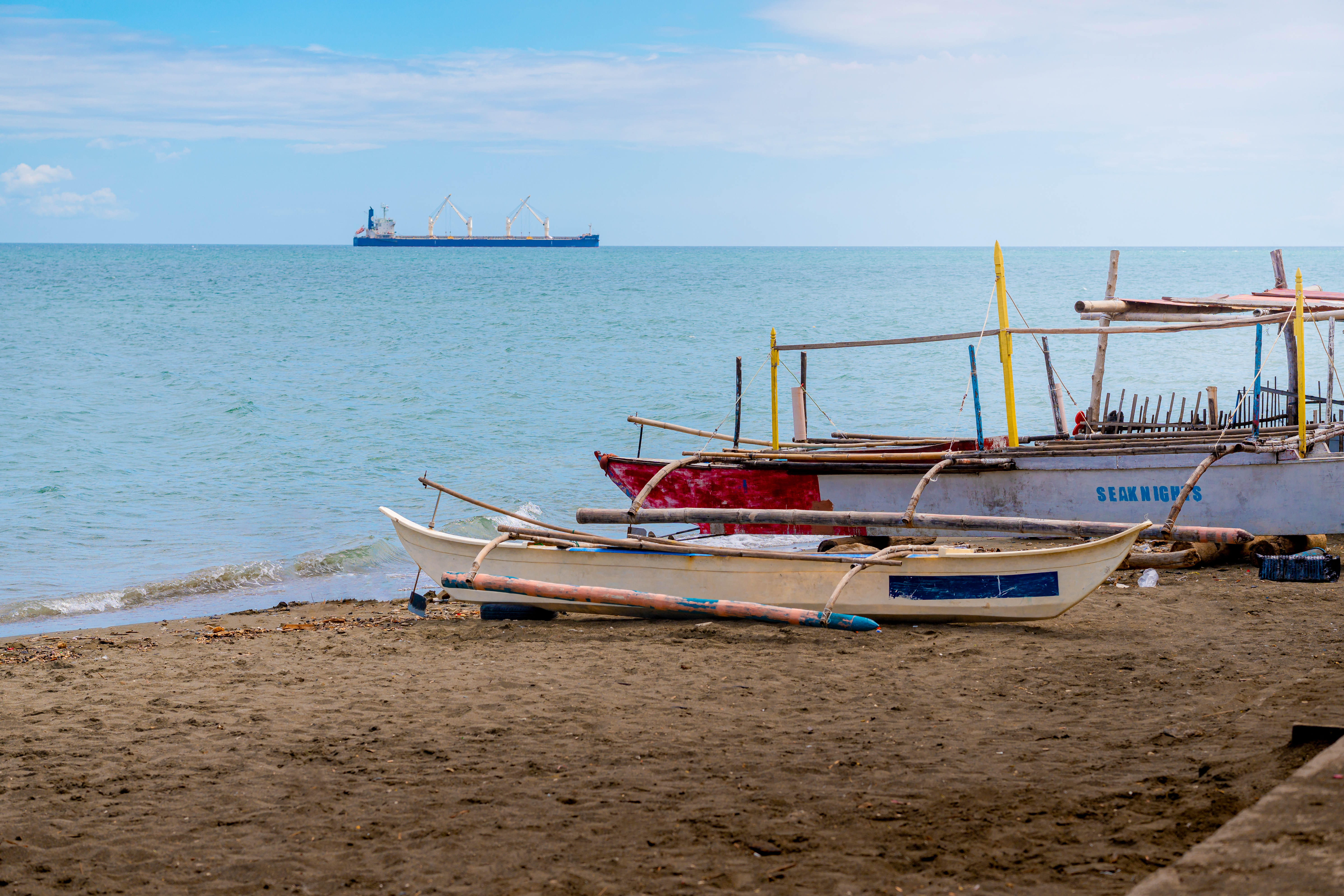 Colorful traditional boats on Talisay beach, Philippines with a cargo ship on the horizon.