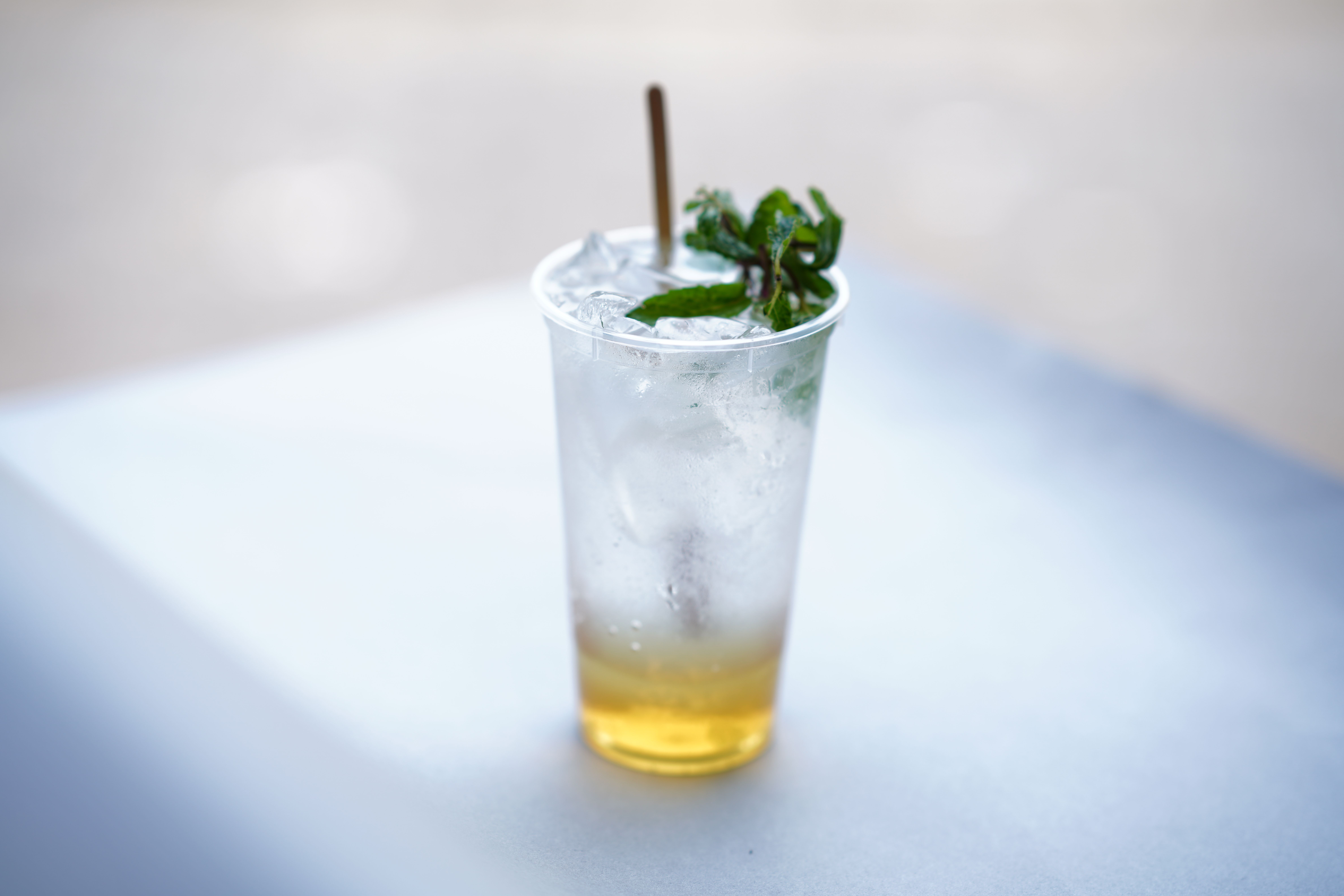 Chilled iced mint lemonade with mint garnish in a clear plastic cup on a sunny day.