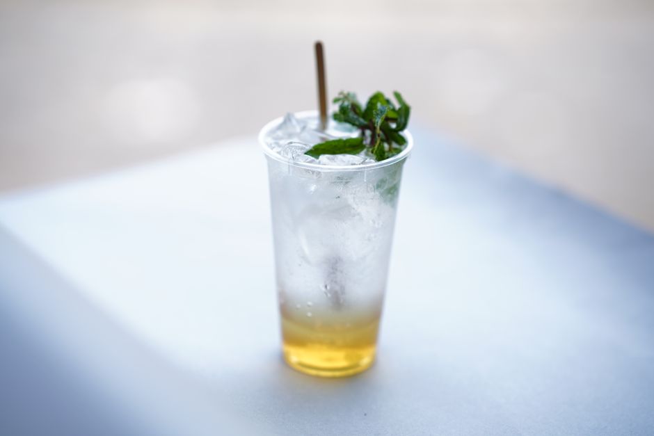 Chilled iced mint lemonade with mint garnish in a clear plastic cup on a sunny day.