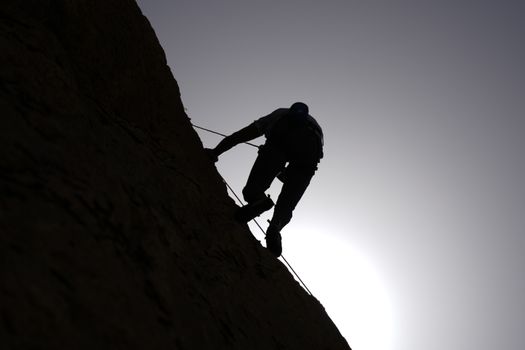 Silhouette of a climber scaling a rocky wall against the rising sun in Damascus, Syria.
