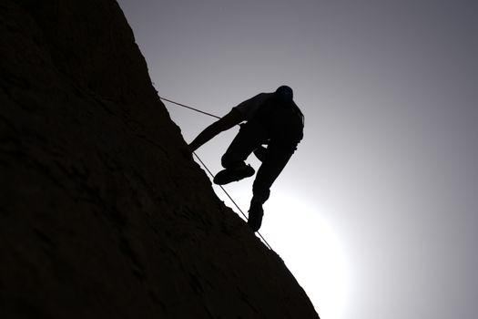 Dramatic silhouette of a climber scaling a rocky cliff with sunlight behind.