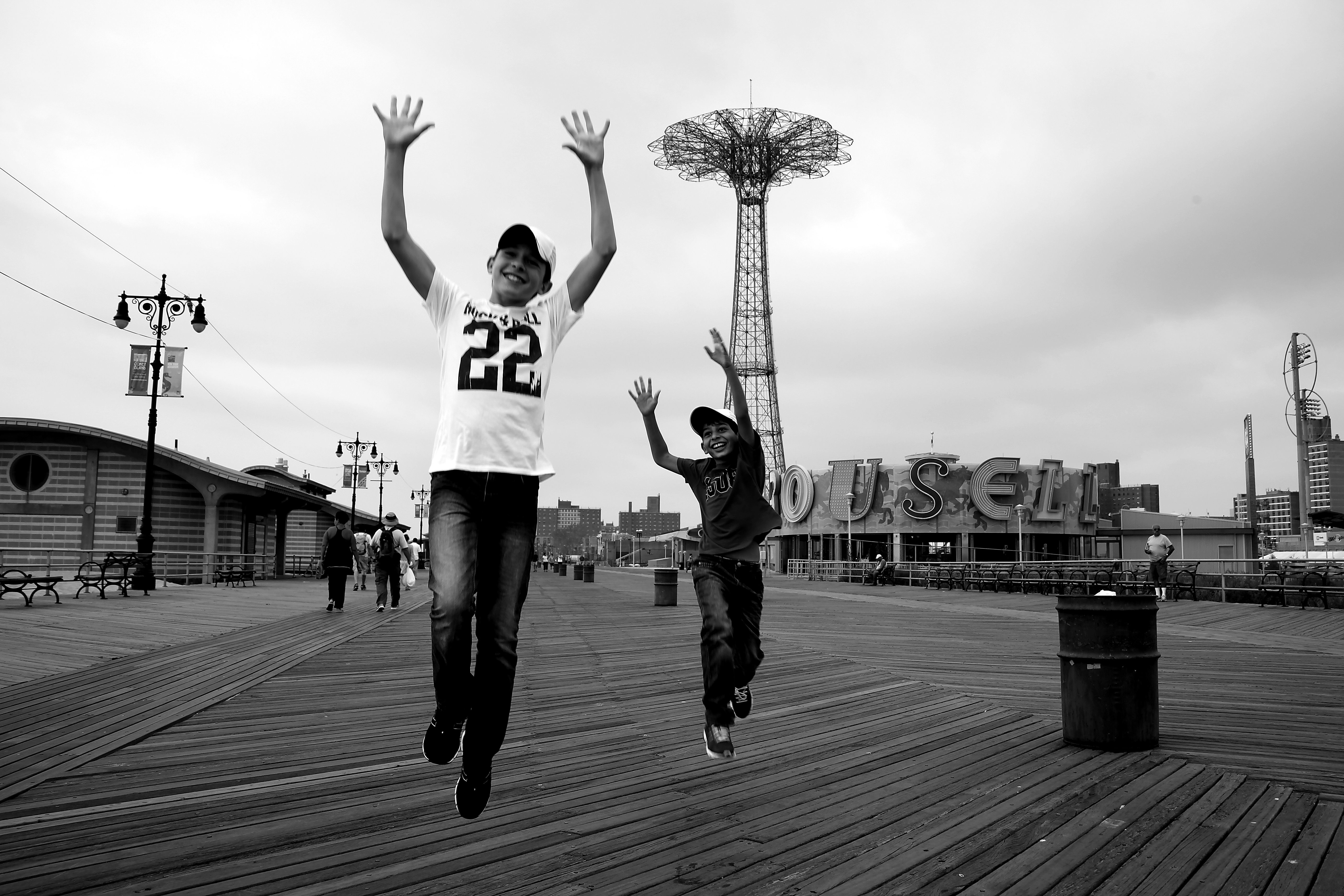 Two young boys joyfully jump on the iconic Coney Island boardwalk in New York City.