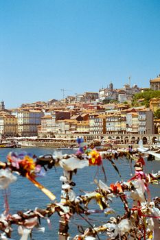 Colorful city buildings by the river with love locks on a fence in the foreground.