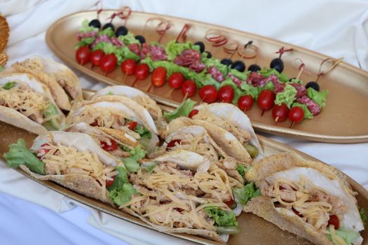 Golden platters featuring tacos with cheese and meat skewers garnished with fresh vegetables.