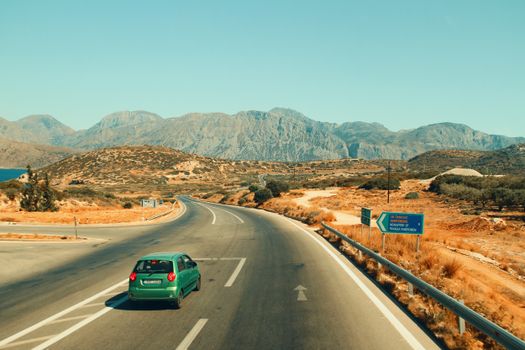 A lone car travels on a winding road through Greece with mountains.