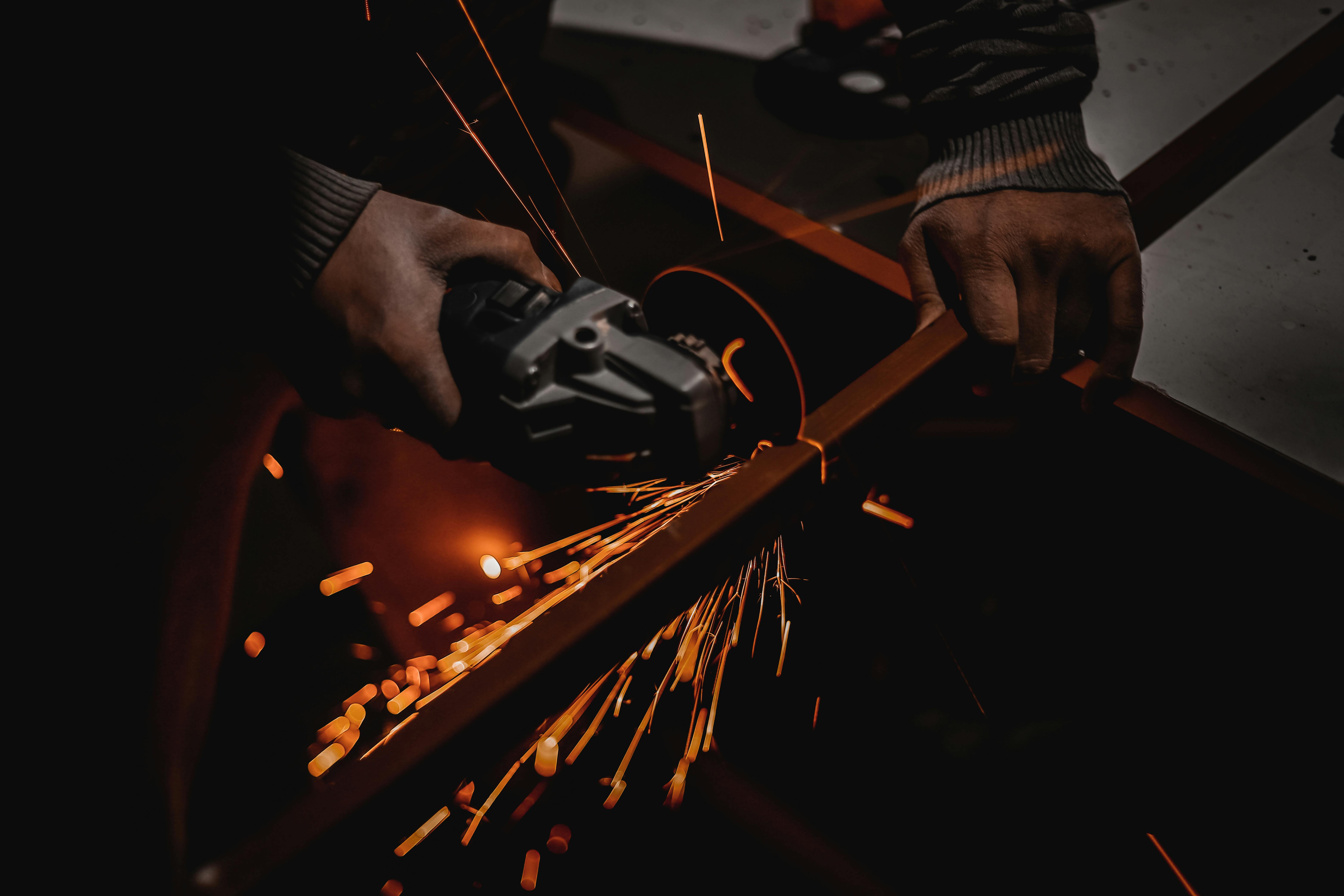 A worker using an angle grinder creates vibrant sparks in a dark workshop setting.