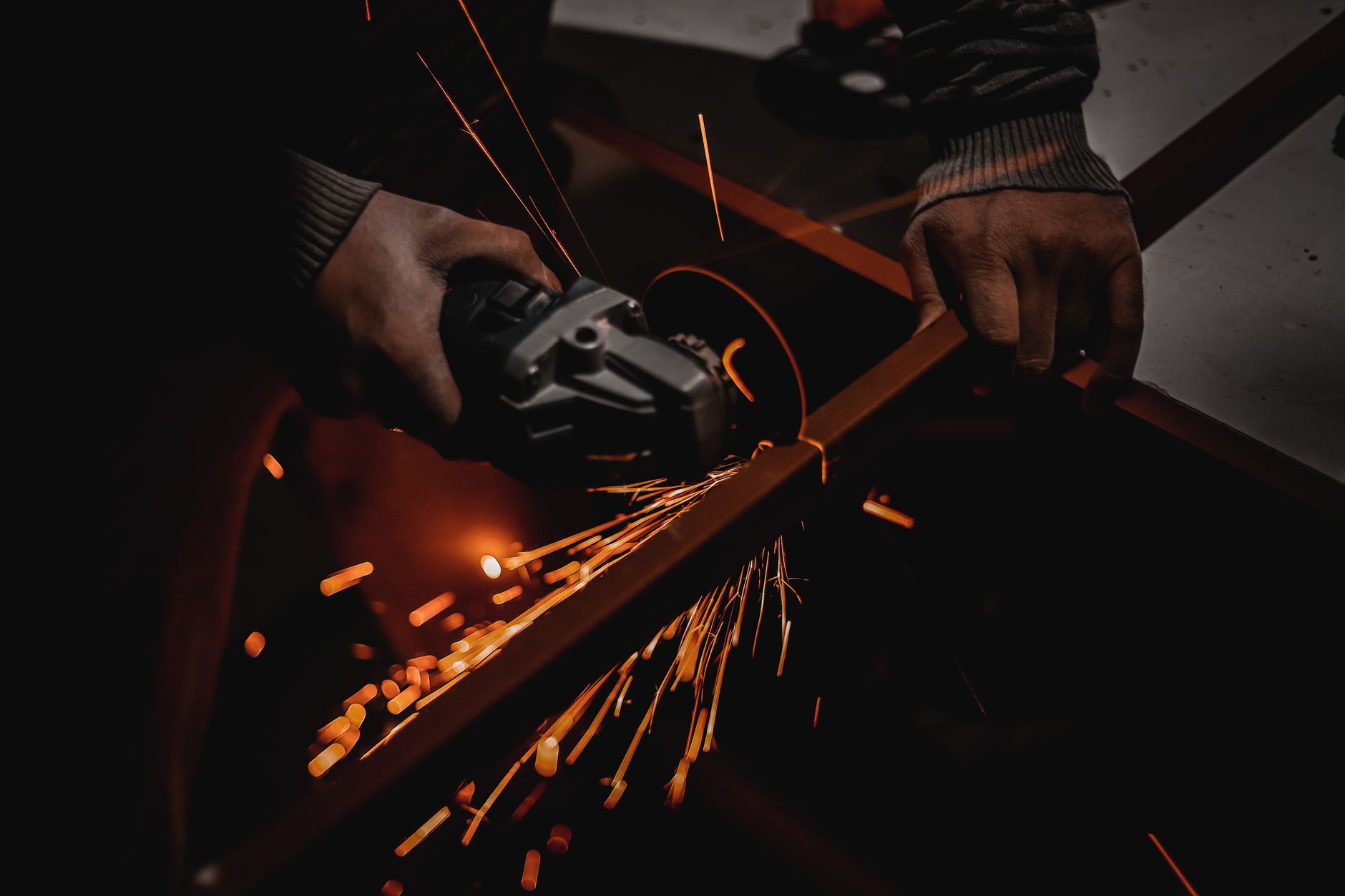 A worker using an angle grinder creates vibrant sparks in a dark workshop setting.