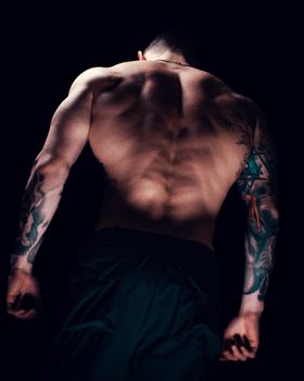 A muscular man with tattoos under dramatic lighting, showcasing strength and art.