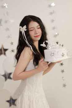 A young woman in a white dress holding a decorative cake indoors with star decorations.