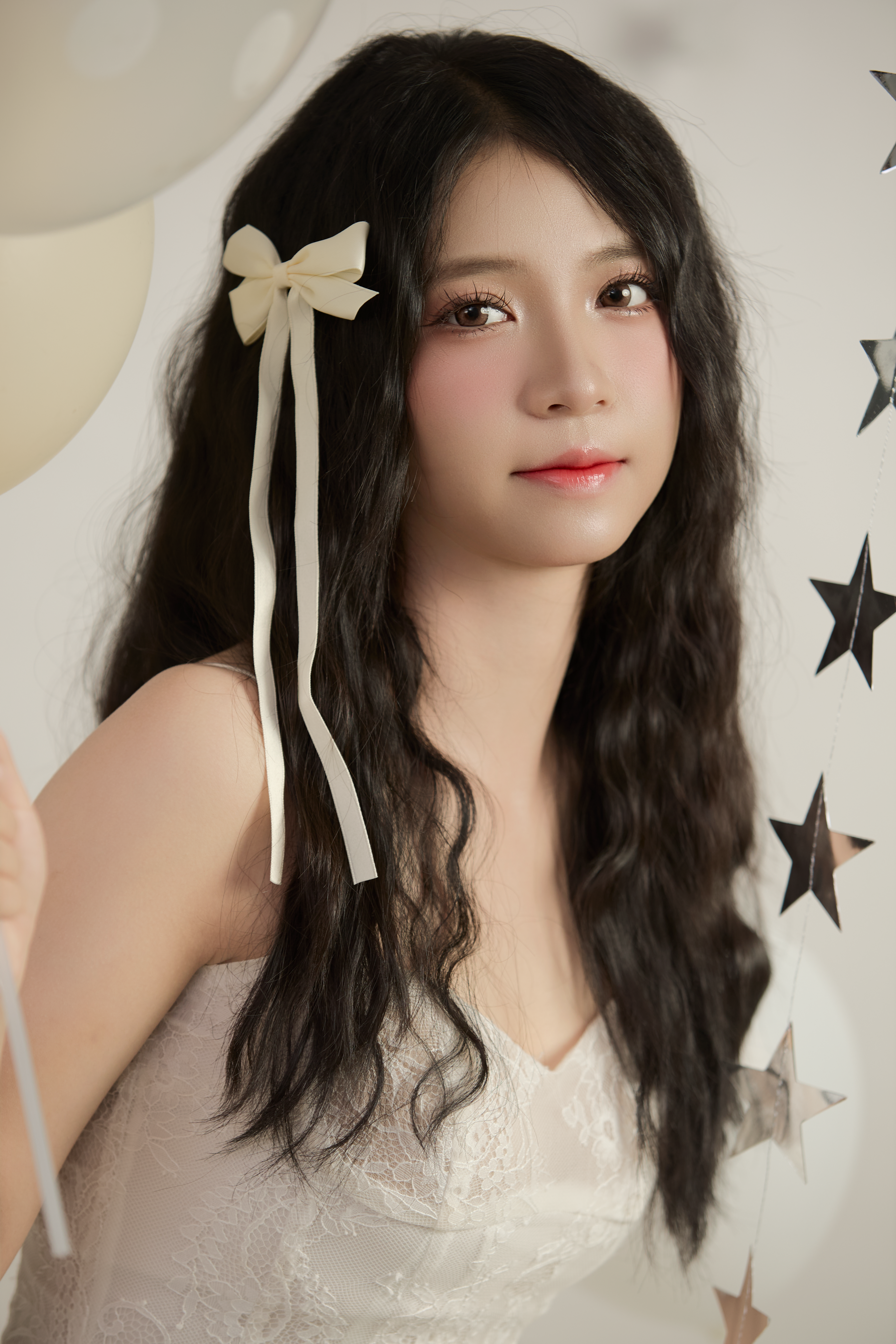 Portrait of a young woman in an elegant white dress holding balloons indoors.