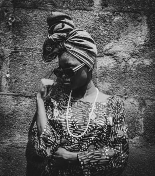 Stylish portrait of a woman in sunglasses and headscarf against a textured wall.