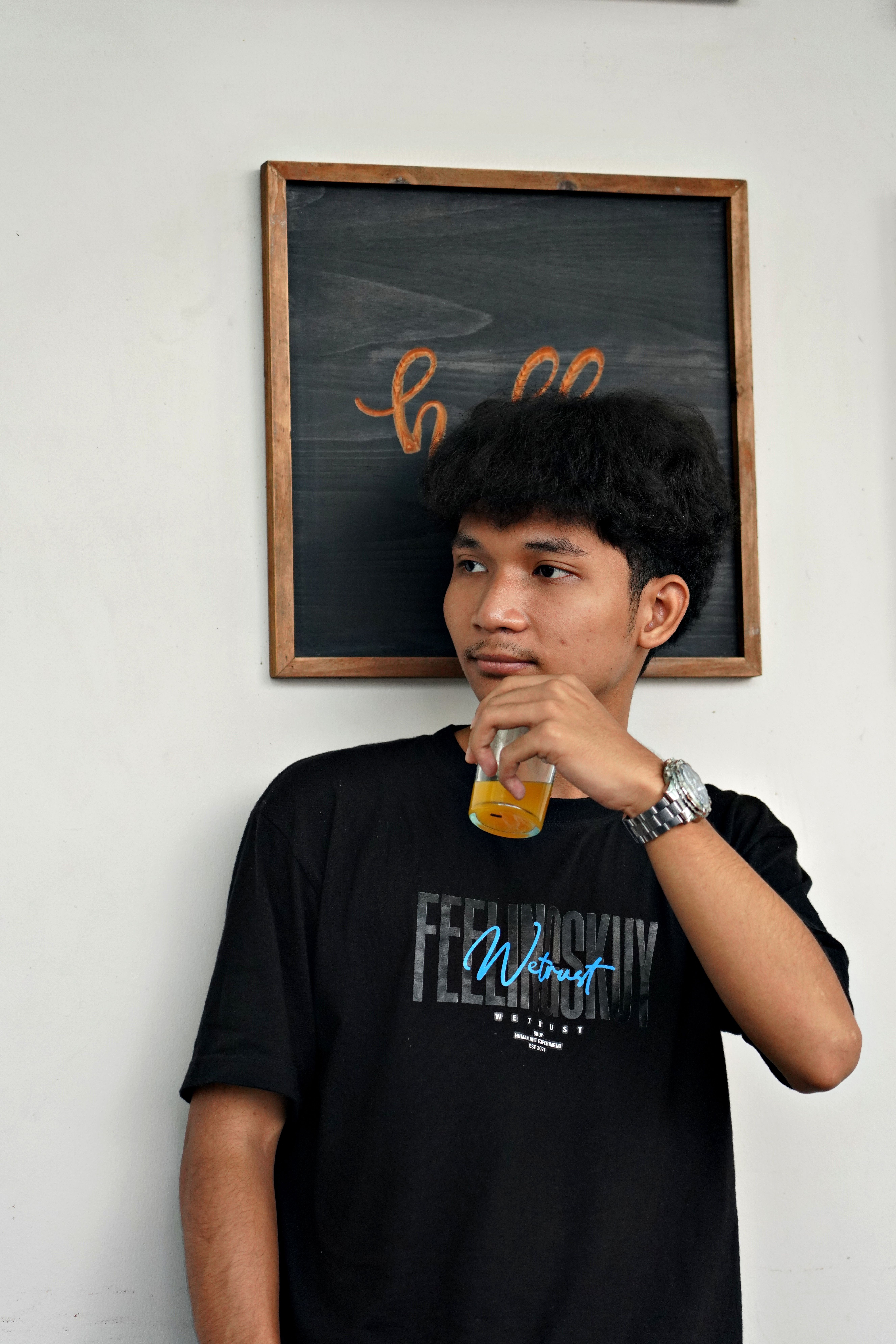 Young man in a stylish T-shirt enjoys a drink in front of a decorated chalkboard.