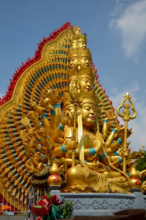 Free Majestic multi-armed Guanyin statue with vibrant gold details against a clear blue sky. Stock Photo