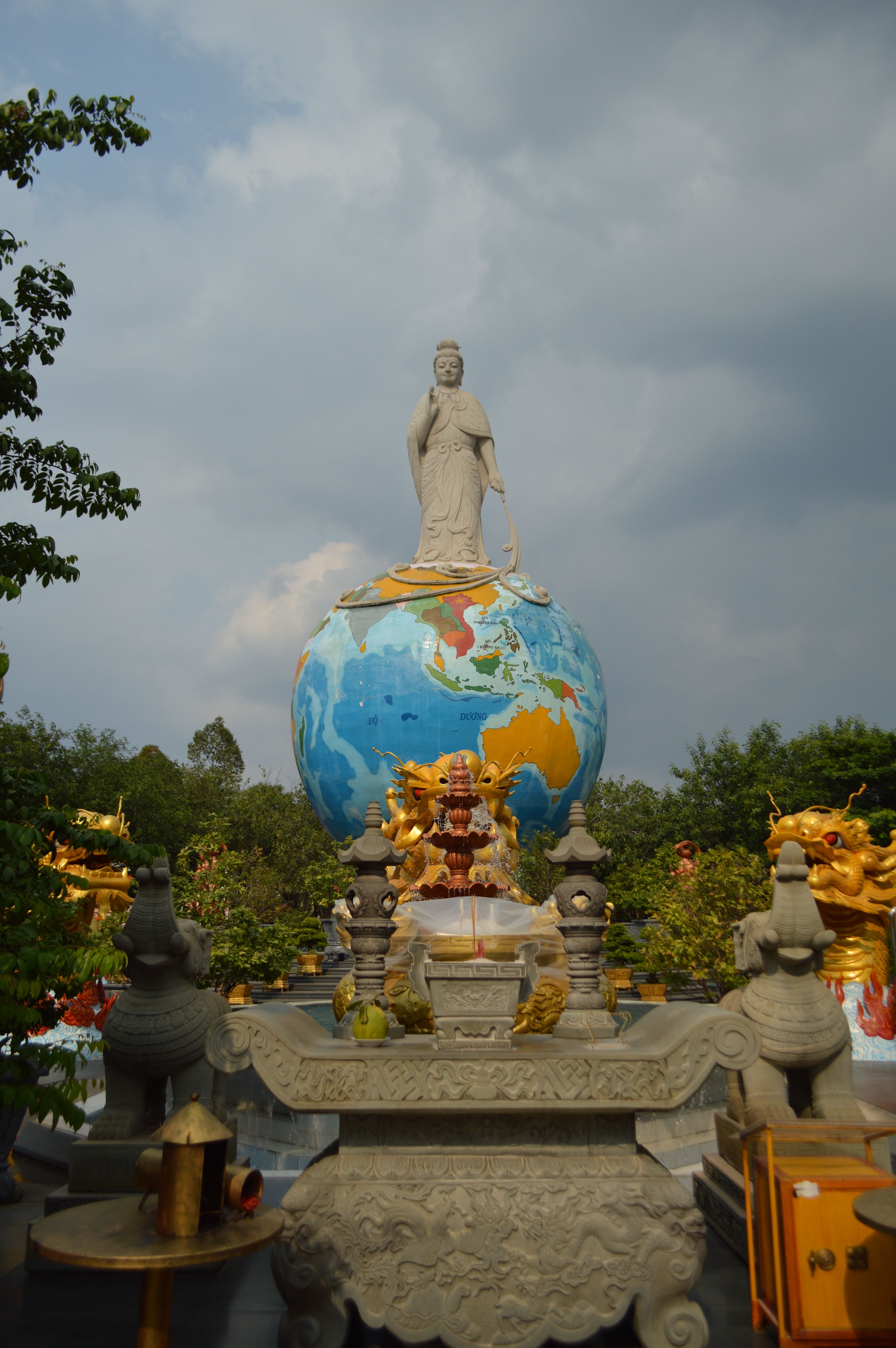 Majestic statue stands atop a globe surrounded by intricate sculptures at an outdoor temple.