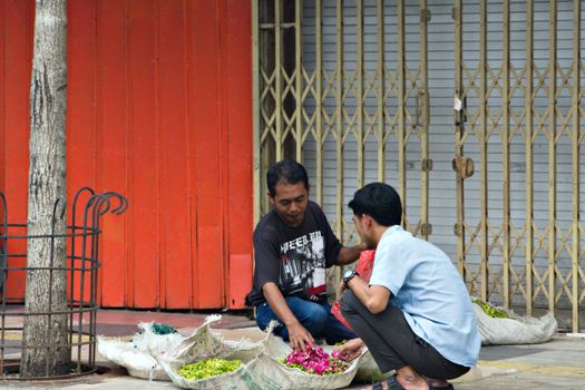 Two men engage in a street market exchange for fresh flowers, vibrant colors evoke local commerce vibe.
