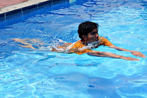 Free A young man enjoying a swim in a clear blue pool on a sunny day outdoors. Stock Photo