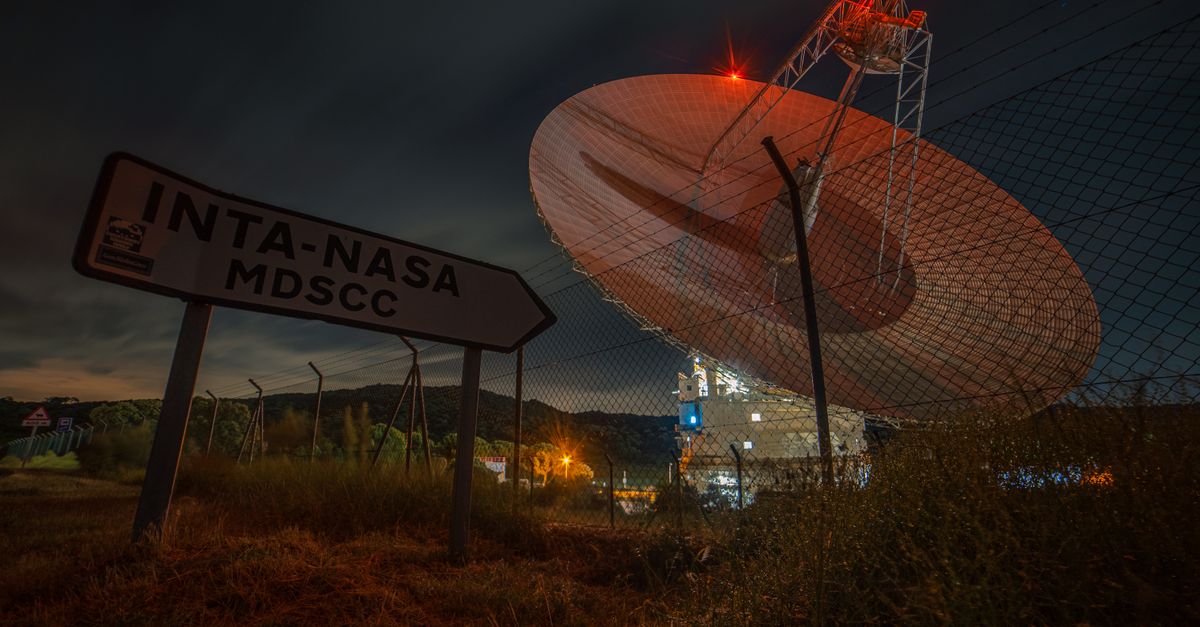 A nighttime view of a satellite dish at Madrid Deep Space Communications Complex under a dark sky.