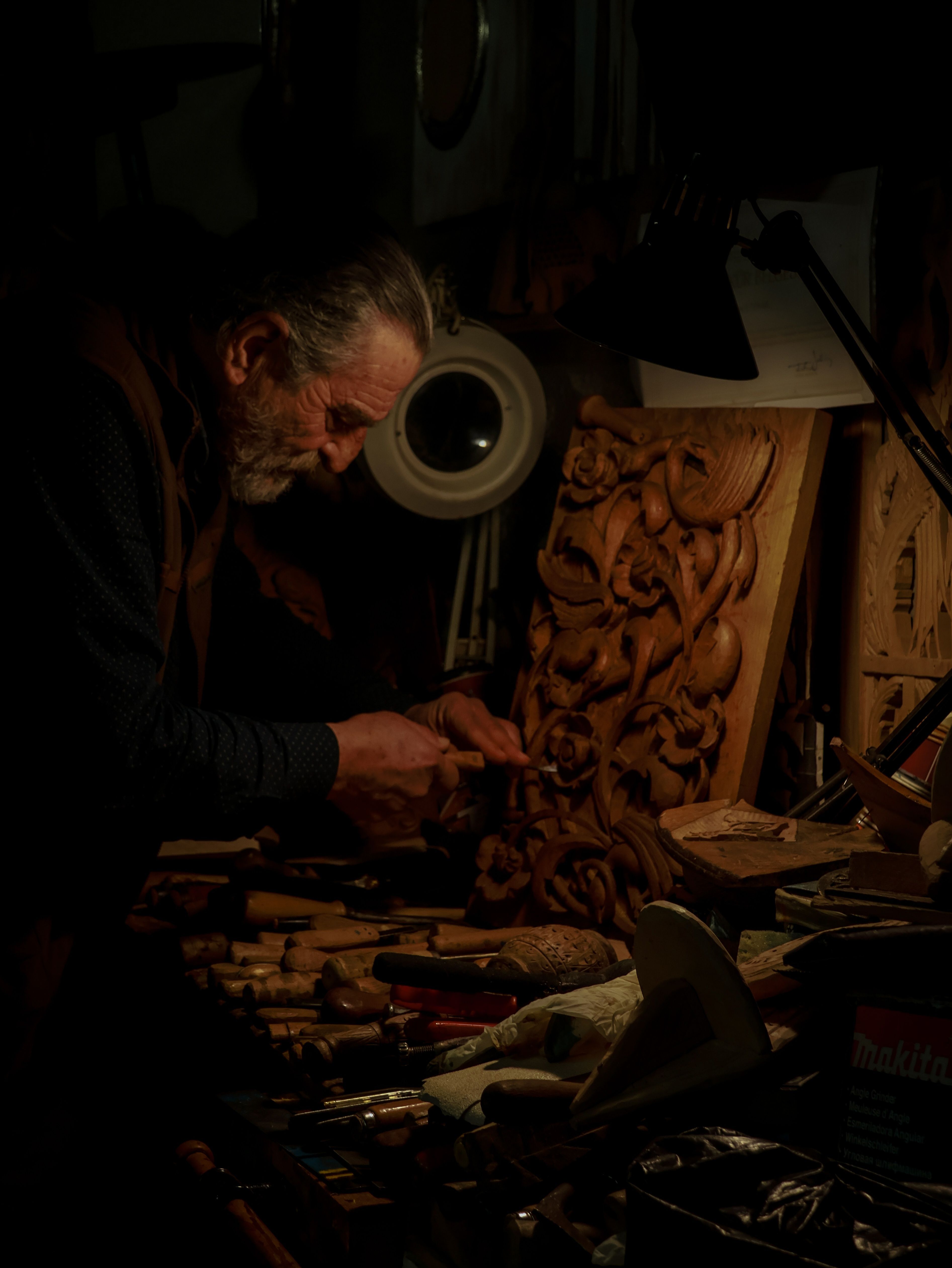 An experienced craftsman meticulously carving wood in a dimly lit workshop, capturing the essence of traditional craftsmanship.