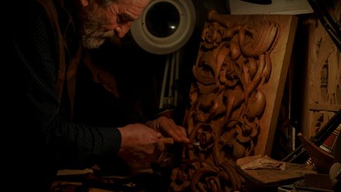 An experienced craftsman meticulously carving wood in a dimly lit workshop, capturing the essence of traditional craftsmanship.