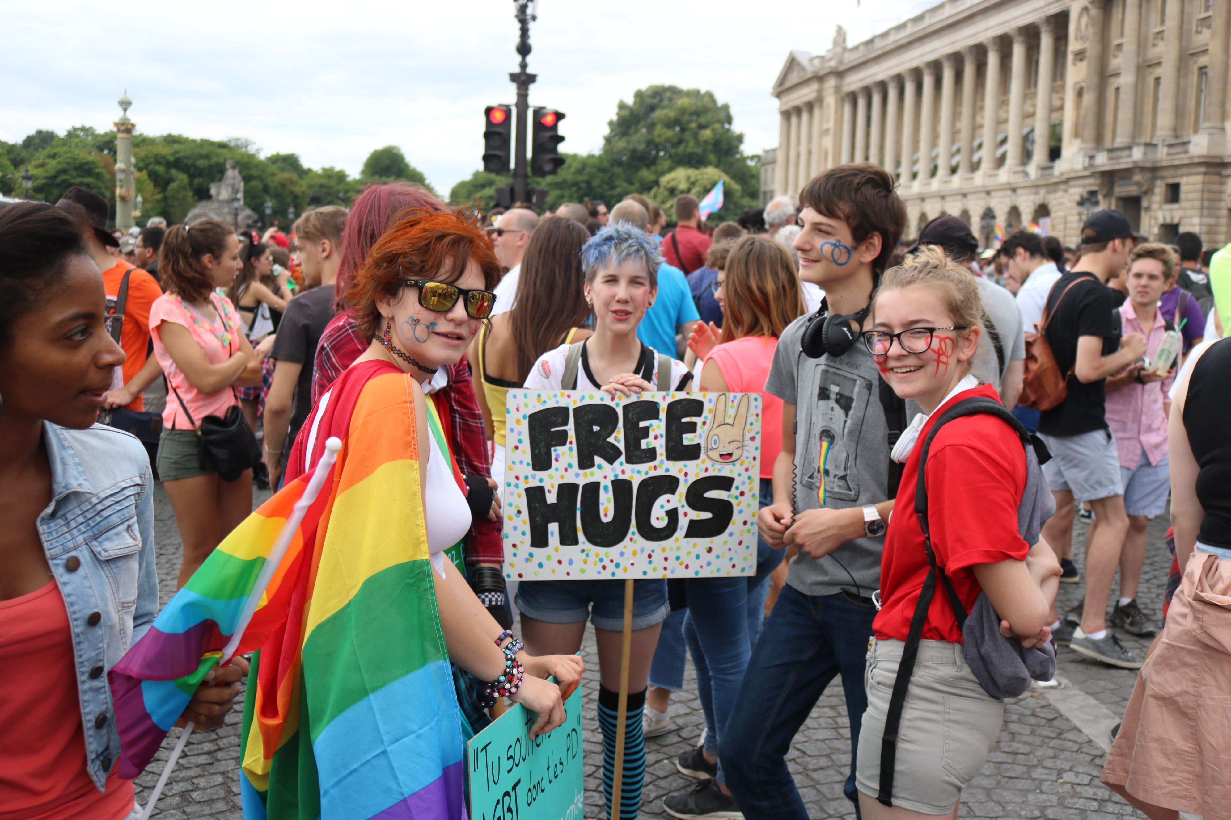 Young participants in a Pride march in Paris, rainbow flag and a "Free Hugs" sign