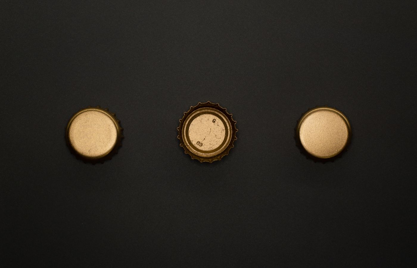 A flat lay showing three gold bottle caps on a black surface, perfect for template and design use.