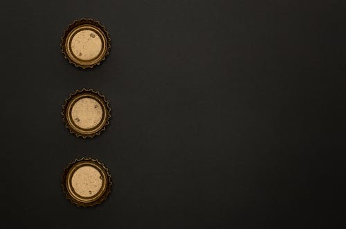 Three Gold Round Bottle Tops on Black Surface
