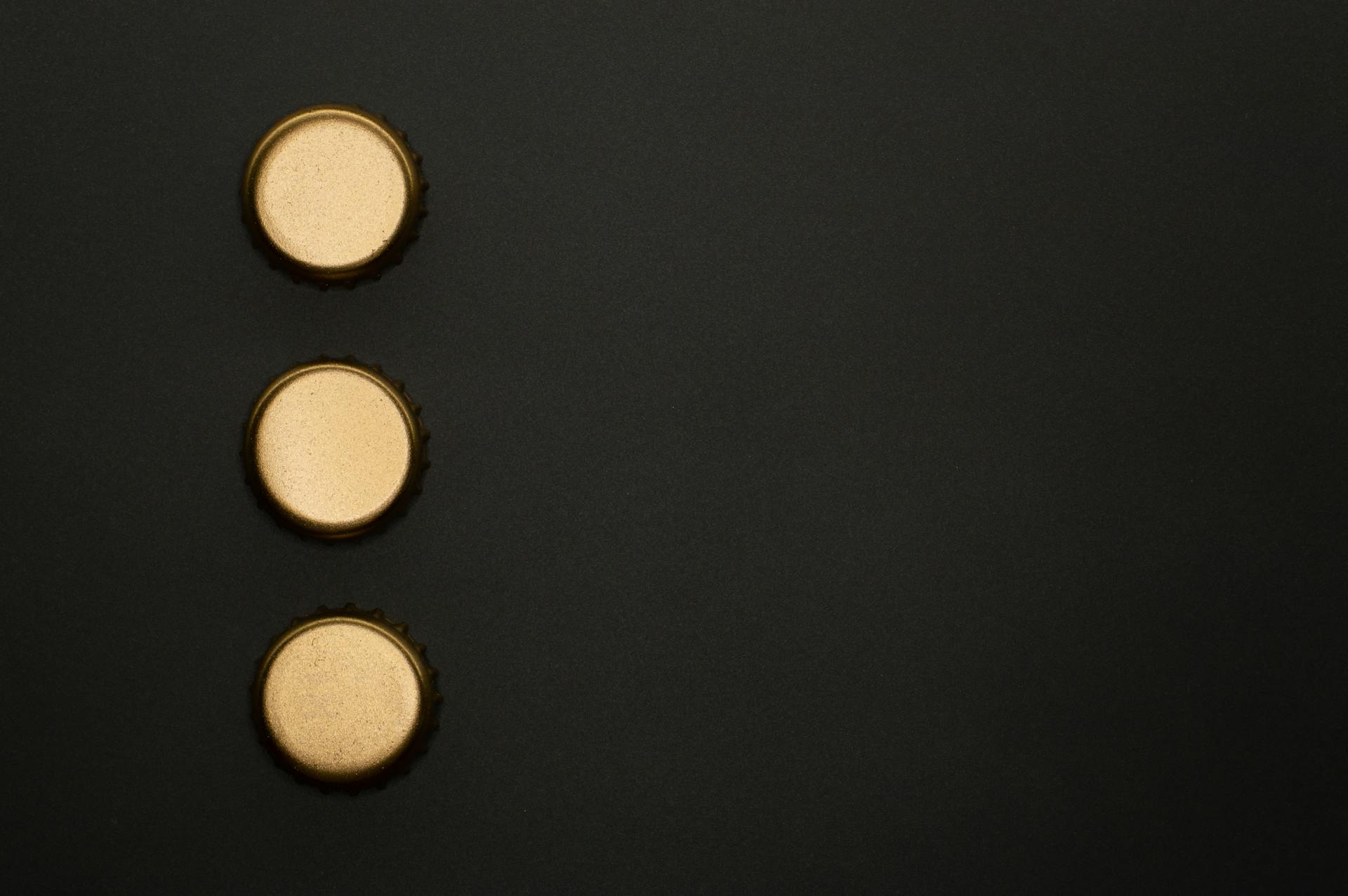 Three golden bottle caps aligned vertically on a black background with ample copy space.