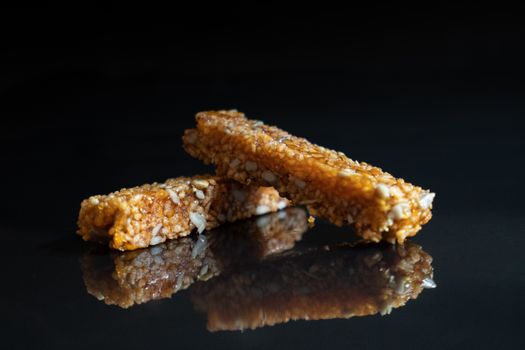 Appetizing nut brittle with fried nuts and honey placed on reflective black surface in dark room
