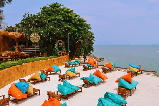 Vibrant beach scene in Thailand with colorful loungers, turquoise sea, and green foliage, perfect for relaxation.