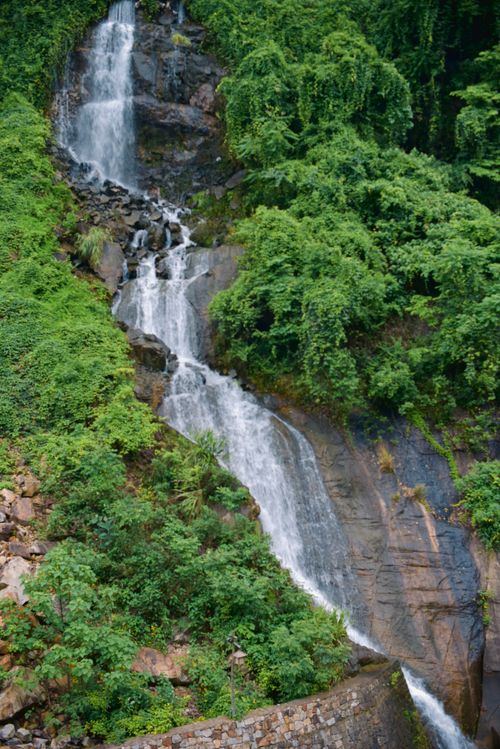 Free A beautiful waterfall cascades down rocks enveloped by dense green vegetation. Stock Photo